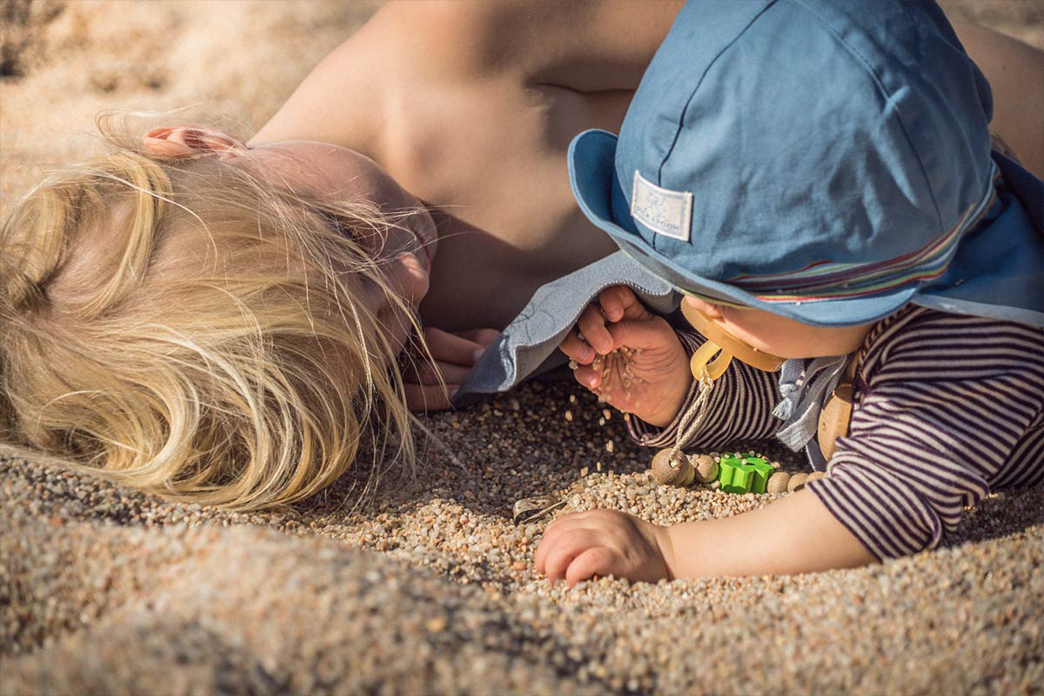 LIFE-for-FIVE-Sardinien-mit-Kindern-Unser Baby und unsere Mittlere liegen am Strand und spielen mit dem Sand.