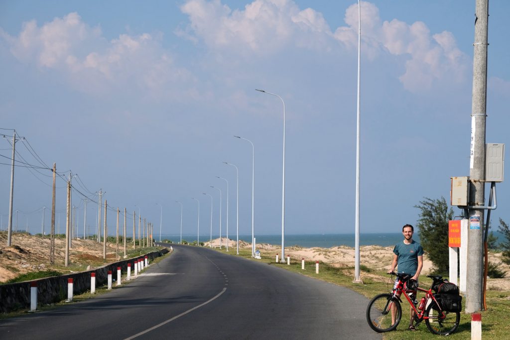 Sebastian steht mit seinem Fahrrad am Rand einer Küstenstraße in Vietnam.