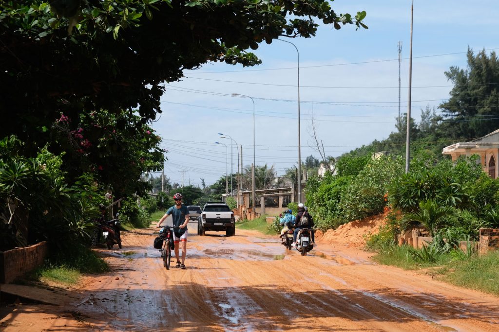 Sebastian schiebt sein Fahrrad in Vietnam über eine mit Schlamm bedeckte Straße.